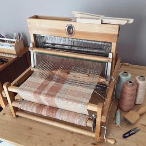 A picture of a four-shaft table loom set up to weave a striped cotton scarf